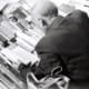 Bureau ou salle de réunion feutrée, lumière naturelle froide, ambiance alpine ou helvétique implicite. Un dirigeant en costume sobre concentré sur des documents financiers ou une analyse, sans sourire commercial.